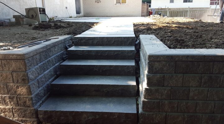 Landscaping Toronto - Concrete staircase flanked by stone walls leading to a paved walkway in a yard under construction, featuring cost-effective natural stone steps.