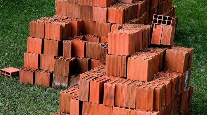 Landscaping Toronto - Stacks of red bricks on a grassy lawn, prepared for bricklaying, some intact and others slightly displaced.