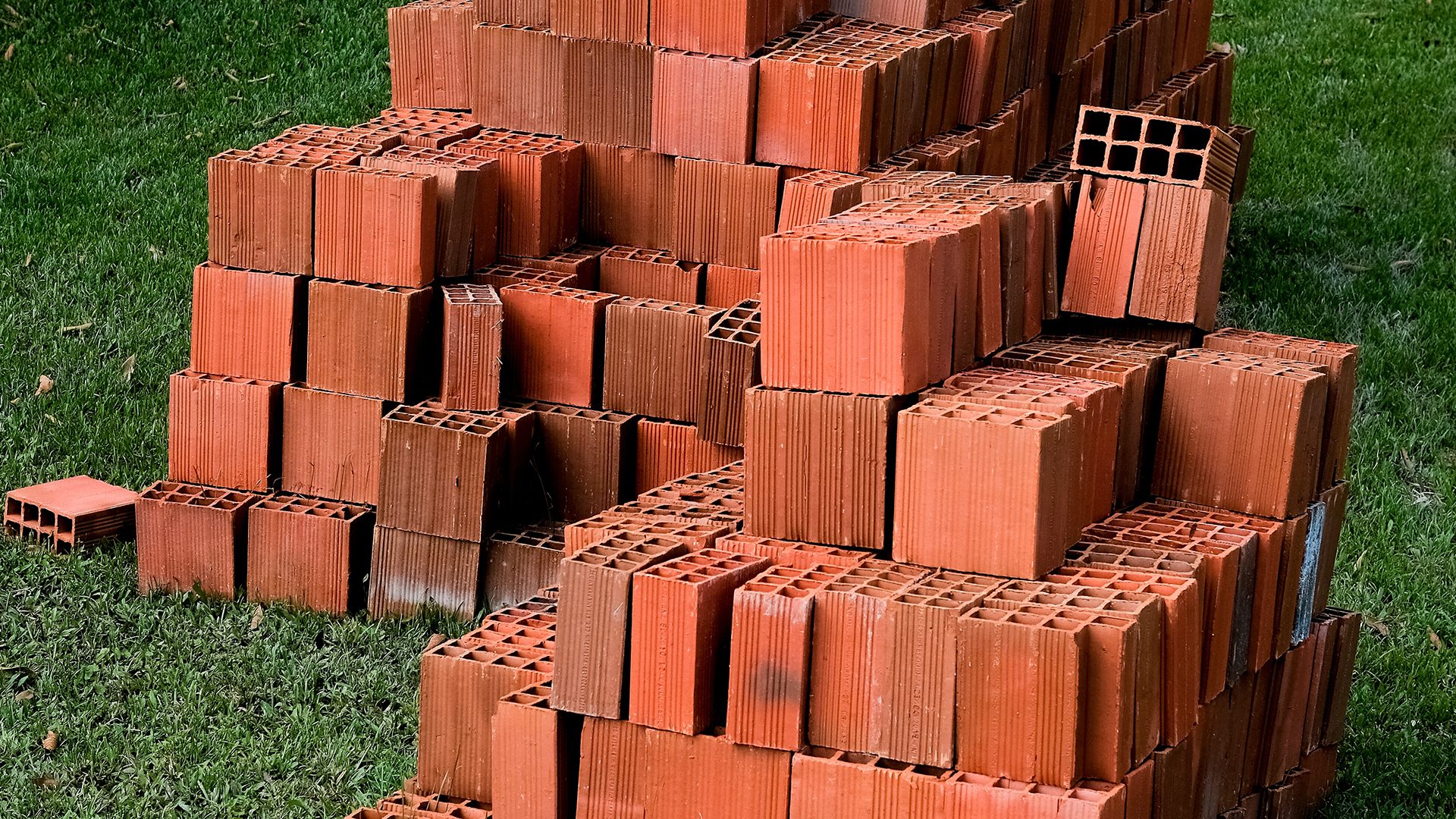 Landscaping Toronto - Stacks of red bricks on a grassy lawn, prepared for bricklaying, some intact and others slightly displaced.