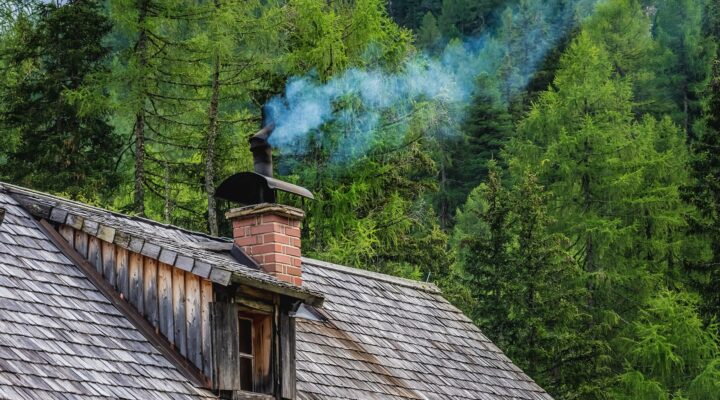 Landscaping Toronto - A rustic wooden cabin with a smoking chimney set against a dense forest of green pine trees, raising the question: how much does a chimney cost?